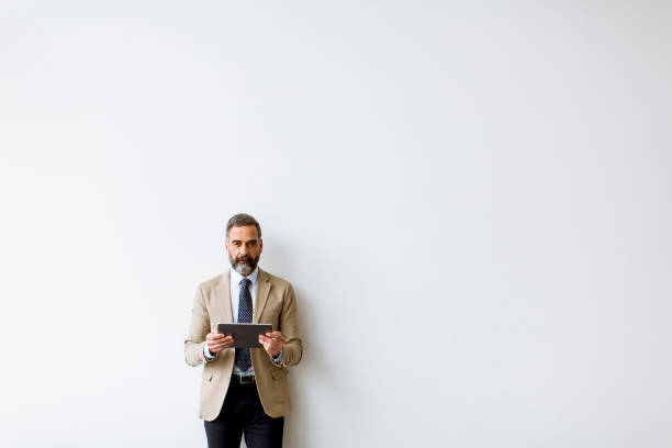 istock Handsome senior businessman with tablet by wall 1186750369