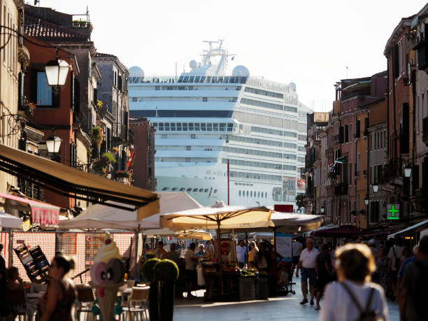 Venice, Italy - June 29, 2019: A huge cruise ship belonging to MSC Cruises entering Venice on the Giudecca Canal, as seen from via Garibaldi (Biennale garden area) of Venice, Italy. Groups of people can be seen canal-side, on a bridge, and on the decks of the boat. Allowing large ships in the delicate Venetian lagoon has elicited controversy and protest.