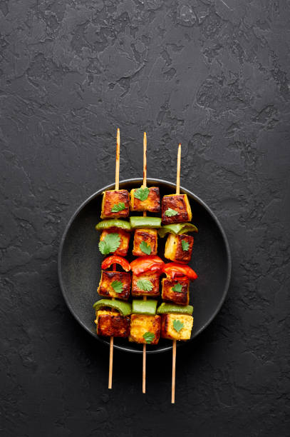 Paneer Tikka at skewers in black bowl at dark slate background. Paneer tikka is an indian cuisine dish with grilled paneer cheese with vegetables and spices. Indian food. Top view. Copy space Paneer Tikka at skewers in black bowl at dark slate background. Paneer tikka is an indian cuisine dish with grilled paneer cheese with vegetables and spices. Indian food. Top view. Copy space marinated photos stock pictures, royalty-free photos & images