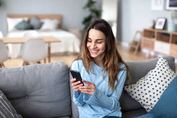 istock Cheerful young woman using mobile phone while sitting on a couch at home. 1186762515