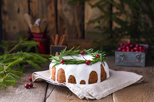 Traditional homemade Christmas fruit cake on the wooden background with fir-tree branches, decorated by cranberries and rosemary, with a copyspace