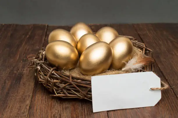 Photo of Nest with golden eggs with a tag and a word retirement on a wooden background. The concept of successful retirement