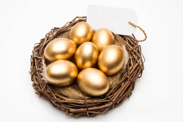 Photo of Nest with golden eggs with a tag and a word retirement on a wooden background. The concept of successful retirement