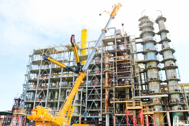 Construction and installation work with a powerful construction crane of a large new industrial oil refining petrochemical chemical plant with pipes, columns, railings, stairs and equipment.