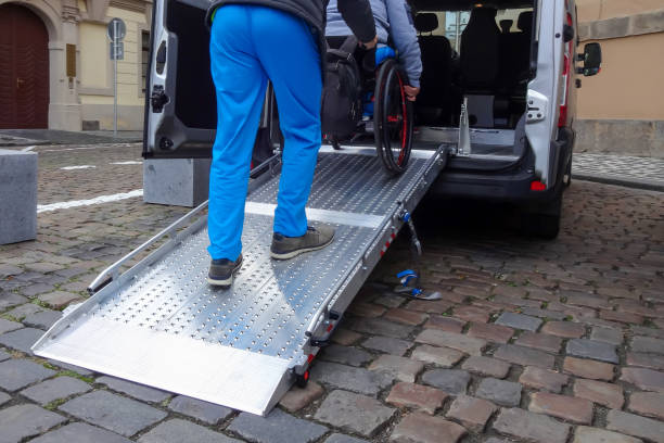 Disabled person on wheelchair using car lift Assistant helping disabled person on wheelchair with transport using accessible van ramp wheelchair lift stock pictures, royalty-free photos & images