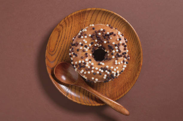 Donut decorated with white and dark chocolate balls on a wooden plate on brown background, top view