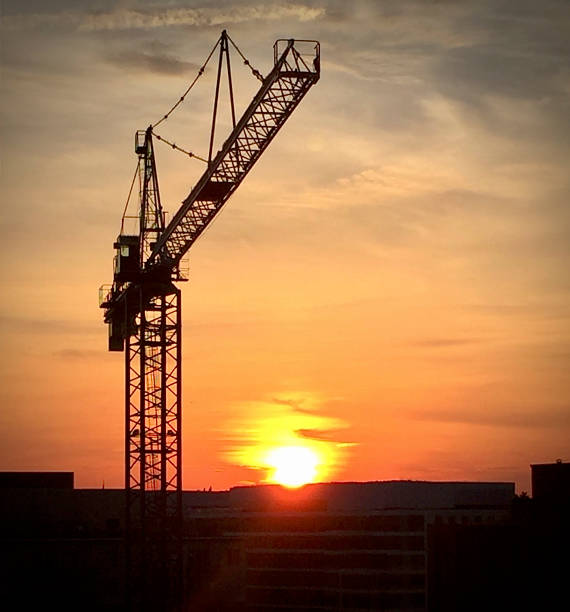 sun setting behind a building while construction is being performed on the roof.
