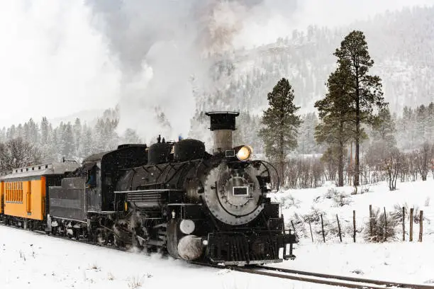 Photo of Vintage Steam Train Billowing Smoke in the Snow as it Moves Through the Mountains.