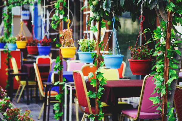 Narrow green street of old Antalya town and rows of tables and different color plant pots outside.