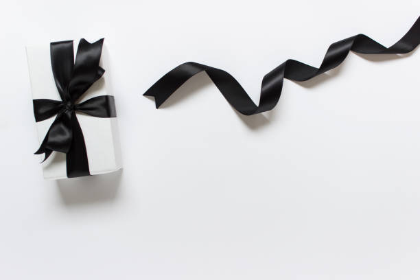 Present wrapped in white paper with black satin bow and black shiny twisted satin ribbon on white background. Photo with copy blank space.