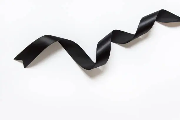 Photo of Black silky ribbon with twists on white background