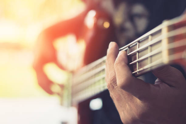 Asian girl child hand holding a 4-string bass guitar with a white color body(focus on fingers).
