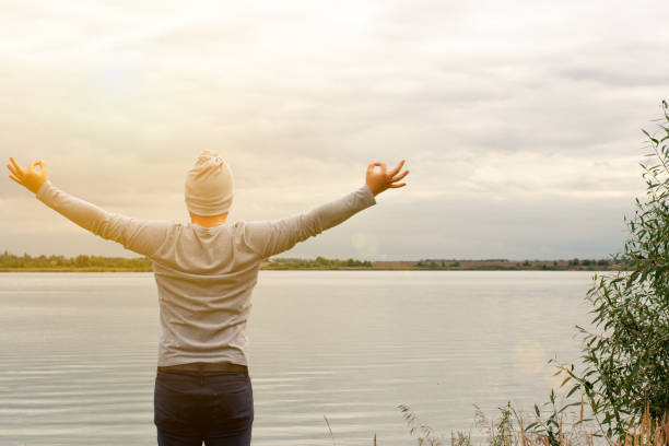 istock A young man is standing on the shore. The view from the back. Yoga classes. Hands raised up. Shows with hands OK sign. Freedom and achievement. 1186803457
