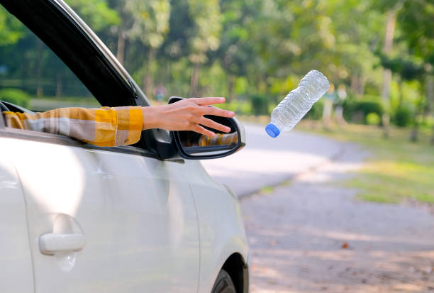 Woman hand throw clear bottle with blue cap out from car window with the concept human garbage destroy environment Woman hand throw clear bottle with blue cap out from car window with the concept human garbage destroy environment. littering stock pictures, royalty-free photos & images
