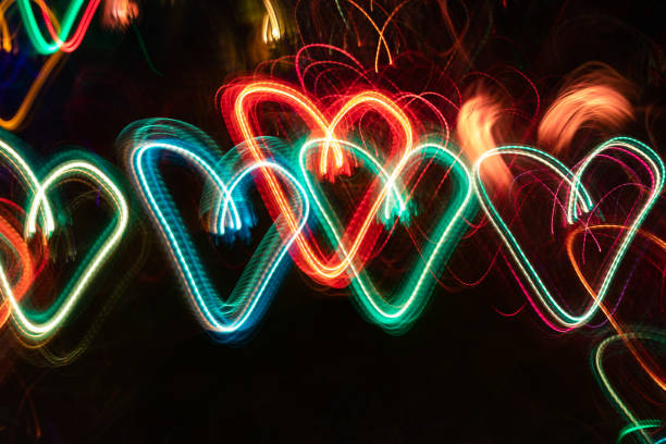 Row of multicolored neon glowing hearts on black background. Abstract luminous neon background. Photographic effect of long exposure while moving.