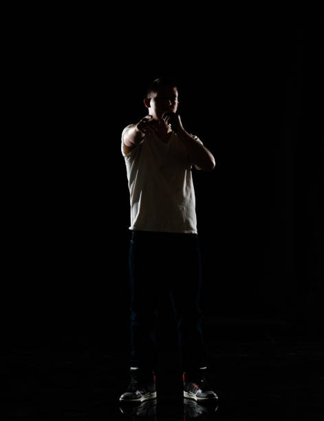 Full length / one man only / one person / front view of 20-29 years old adult handsome people caucasian male / young men singer / musician standing / dancing in front of black background wearing canvas shoe / jeans / pants / t-shirt / shirt who is singing / happy and holding microphone / black color / back lit / hip-hop longitud completa / un hombre solamente / una persona / vista frontal de 20-29 años de edad adulto guapo personas caucásicas hombres / hombres jóvenes cantante / músico de pie / bailando frente al fondo negro usando zapato de lona / jeans / pantalones