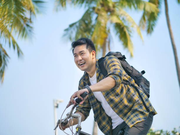 istock Happy Asian man with backpack riding bicycle with green tree 1186824953