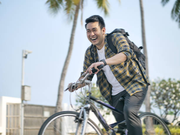 istock Motion blur happy Asian man with backpack riding bicycle with green tree 1186824954