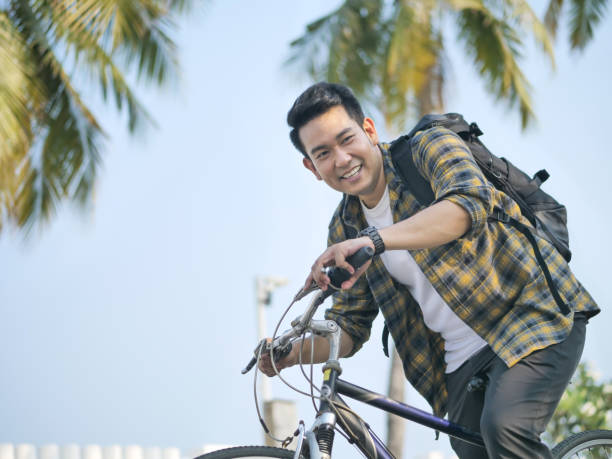 緑の木で自転車に乗ってバックパックを持つ幸せなアジアの男 - campus university walking school ストックフォトと画像