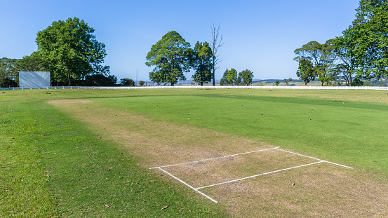 Scenic cricket grounds grass wicket pitch and distant from white boundary fence summer blue day countryside landscape.