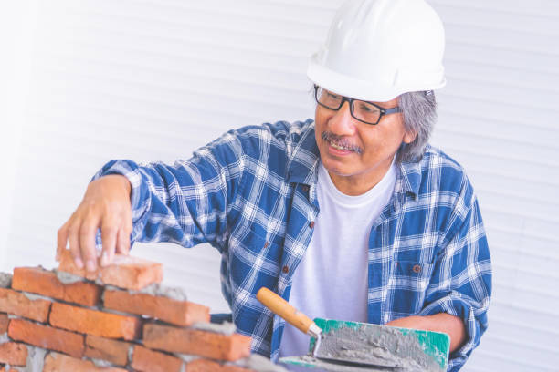 istock Old construction worker is laying down brick wall with cement, wearing protected builder hard hat 1186840378