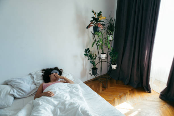 istock woman with sleeping mask in bed morning light through curtains. white sheets 1186842987