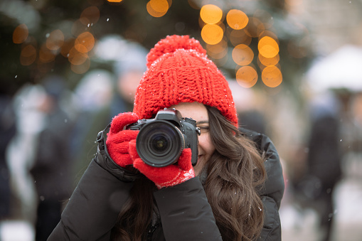 woman photographer with professional camera shooting outdoors at winter time christmas tree on background