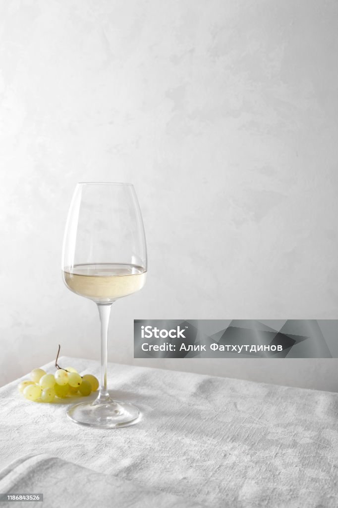 White wine in a glass and a bunch of grapes on the table. Light background. White Wine Stock Photo