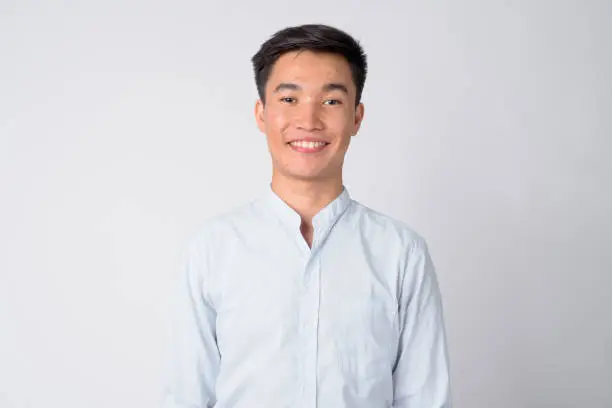 Studio shot of young handsome Asian businessman against white background