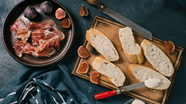 ingredientes para tapas españolas, pinchos o aperitivos bruschetta. sabroso jamón, jamón, baguette, higos, queso y hierbas en la mesa de comedor. - serrano chilli pepper meat ham spain fotografías e imágenes de stock