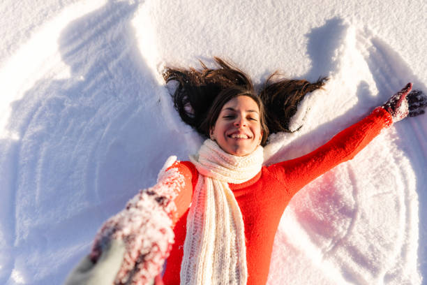 Making snow angels Young cheerful woman is lying in the snow and making snow angel. Person behind a camera helping her to get up. POV concept. snow angels stock pictures, royalty-free photos & images