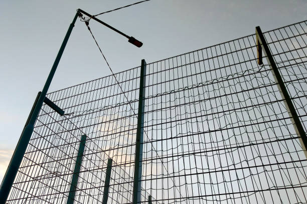 istock High wire mesh fence in restricted area on blue sky background. 1186865176