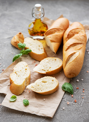 Sliced fresh crusty baguette with salt, olive oil  and basil on a grey concrete background