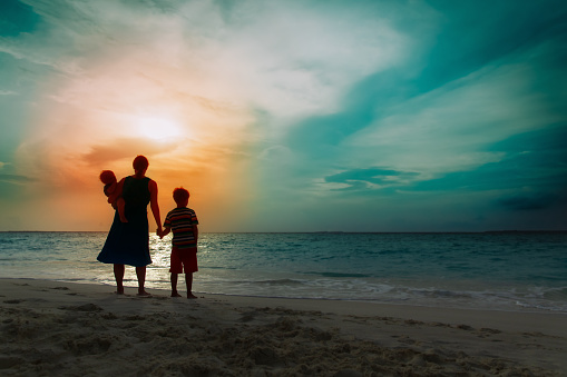 mother and kids looking at sunset on tropical beach vacation