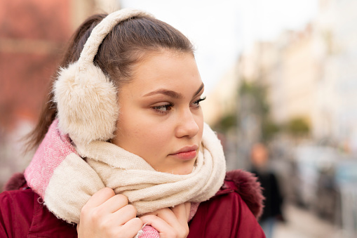An attractive young woman looks sideways outdoors in the city while wearing warm clothes for the winter season.