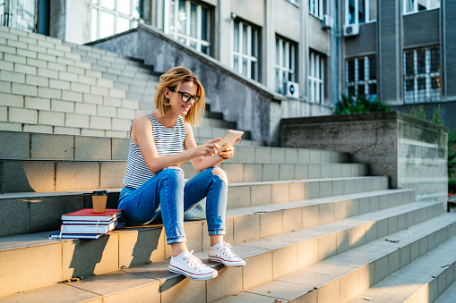 Young beautiful Caucasian female college student using tablet on a staircase.