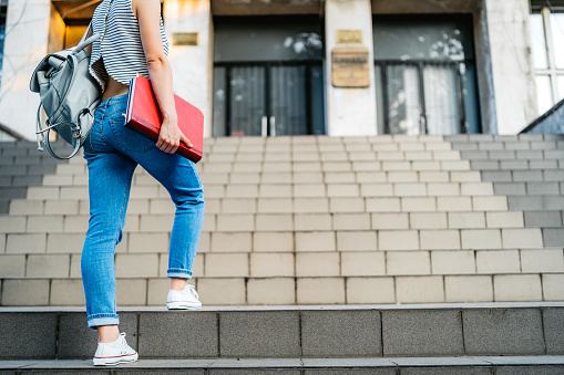 Young Caucasian female college student climbing stairs with books in hand.
