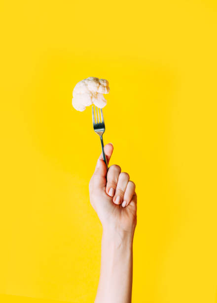 istock Female hand holding fork and cauliflower on it on yellow background. 1186876252