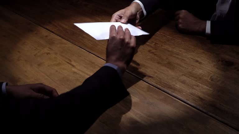 Businessmen in dark room accepting payoff in envelope in deal