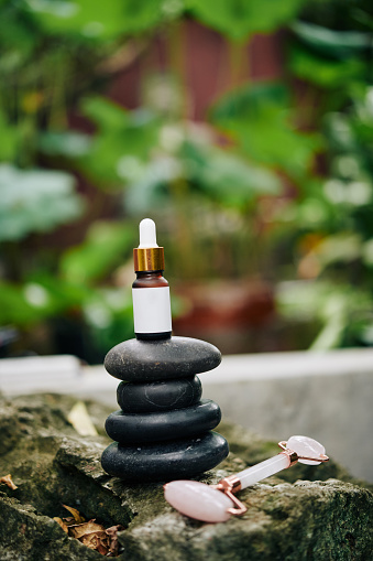 Small bottle of serum on stack of basalt stones and rose quartz face roller