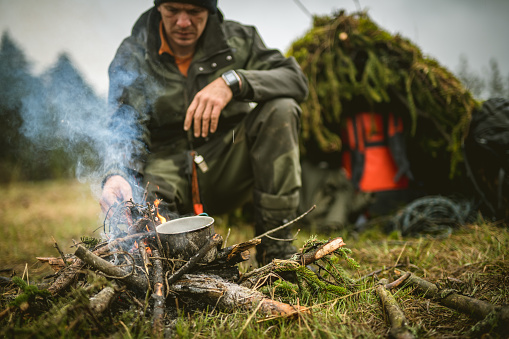 Hiker making tea with leaves on campfire in forest.