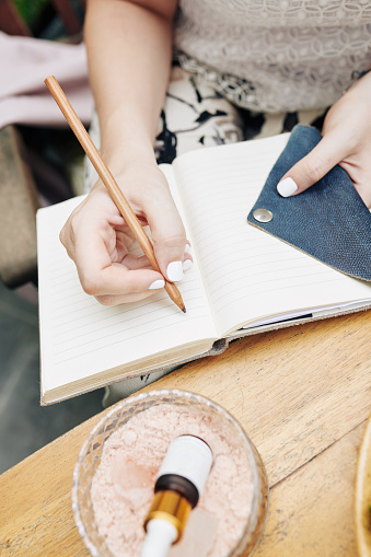 Hands of female entrepreneur writing business plans in notepad when developing cosmetics brand