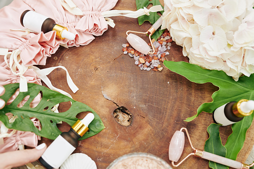 Wood stump with flowers, quartz massage rollers and bottles with essense or natural oil around, view from above