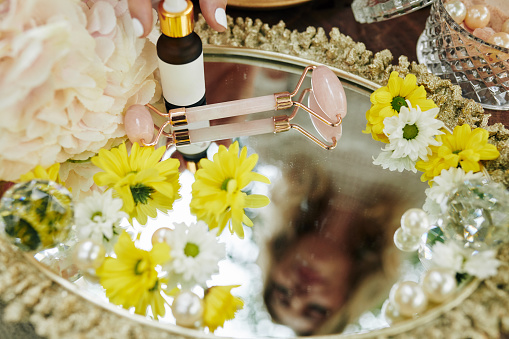 Tray with quartz massage roller, moisturizing essence and flower buds, selective focus