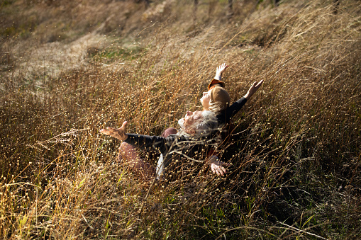 High angle view of happy mature couple sitting in tall grass with their arms outstretched. Focus is on man. Copy space.