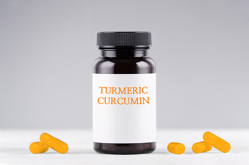 nutritional supplement turmeric curcumin bottle and capsules on gray background