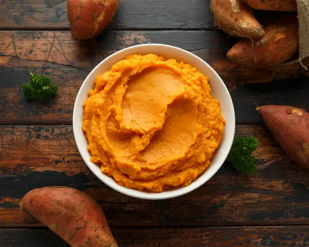 Mashed Sweet Potatoes in white bowl on wooden rustic table. Healthy food.