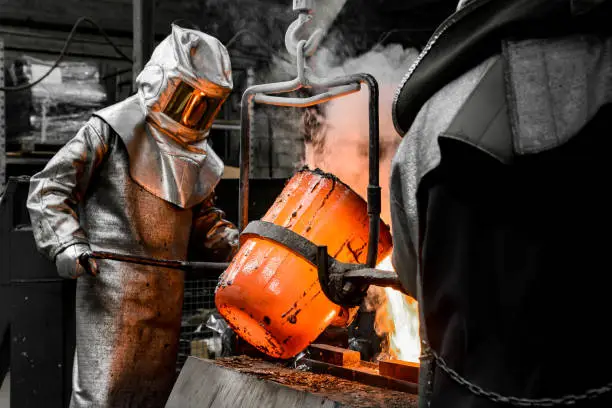 A worker protected by a safety suit pours the molten metal into a mold
