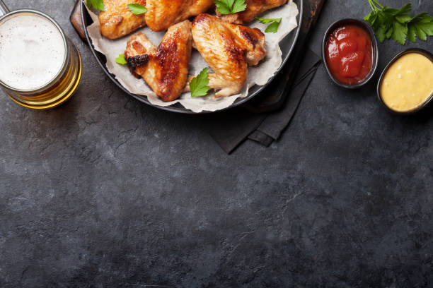 Hot chicken wings and draft beer Hot barbecue chicken wings with sauce and draft beer. Top view on stone table with copy space pub table top view stock pictures, royalty-free photos & images