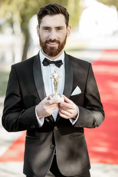 Portrait of an elegant man strictly dressed in tuxedo as a well-known actor standing on the red carpet during the awards ceremony